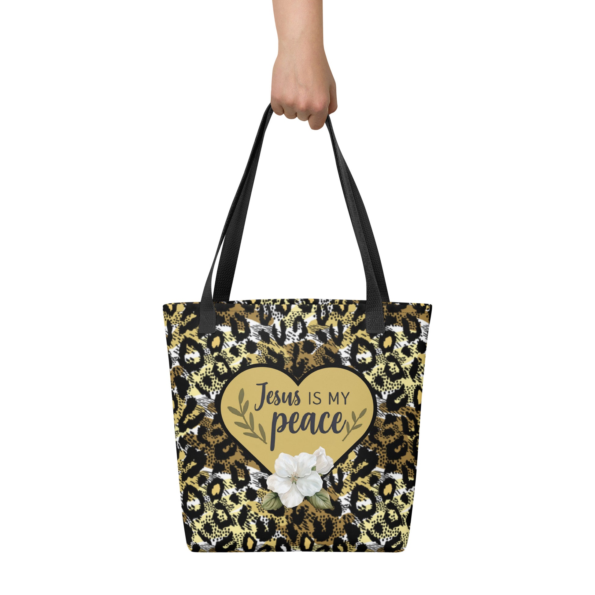 Close-up lifestyle image of the cheetah print Christian tote bag being held by hand, showing the black straps and the centered gold heart design with the words “Jesus is my peace.”