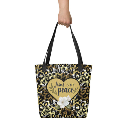 Close-up lifestyle image of the cheetah print Christian tote bag being held by hand, showing the black straps and the centered gold heart design with the words “Jesus is my peace.”