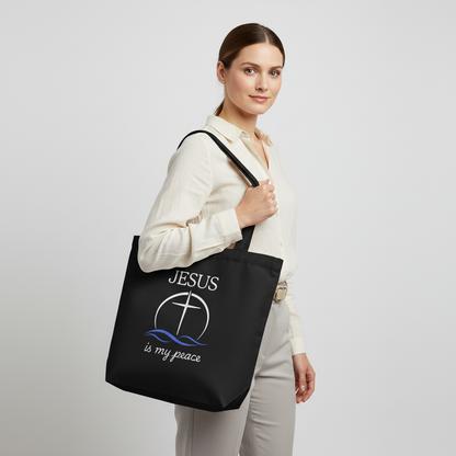 Model holding a black cotton tote bag printed with “JESUS is my peace” and a cross-in-circle with blue waves design.