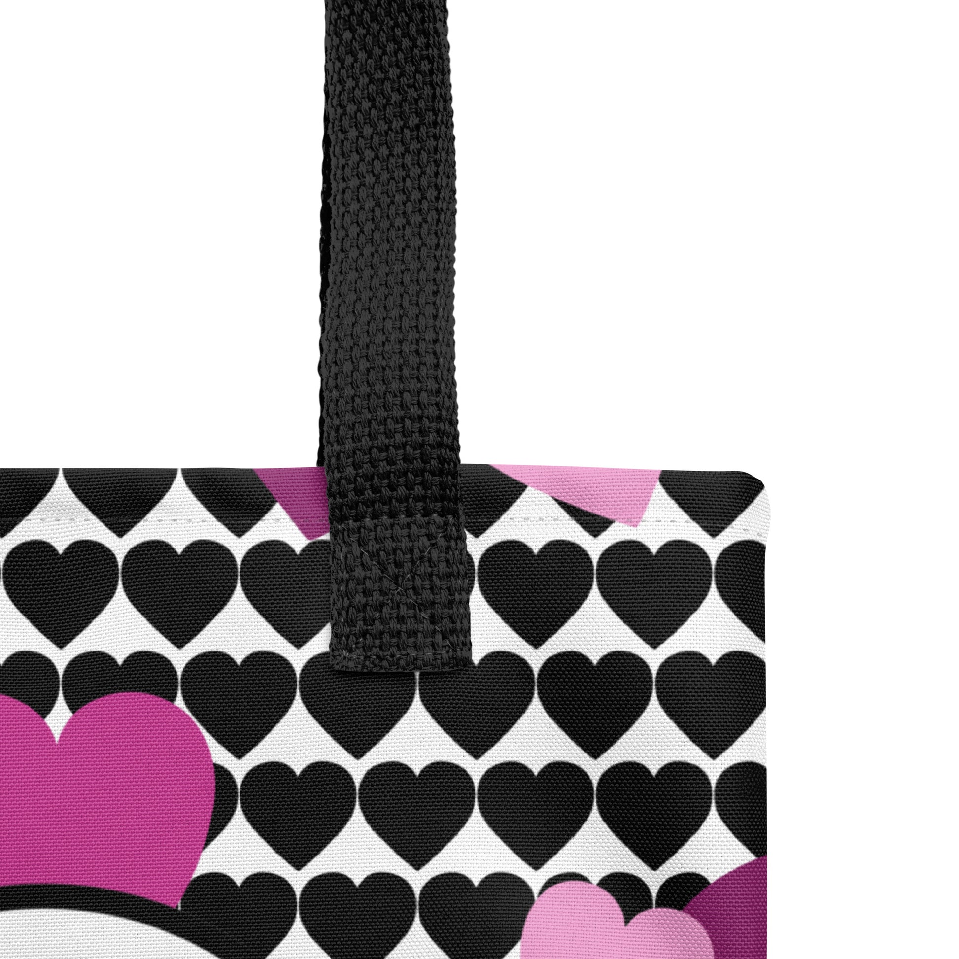 Close-up of the tote’s heart pattern and print texture, highlighting the black straps, white heart graphic, and pink/purple heart accents.