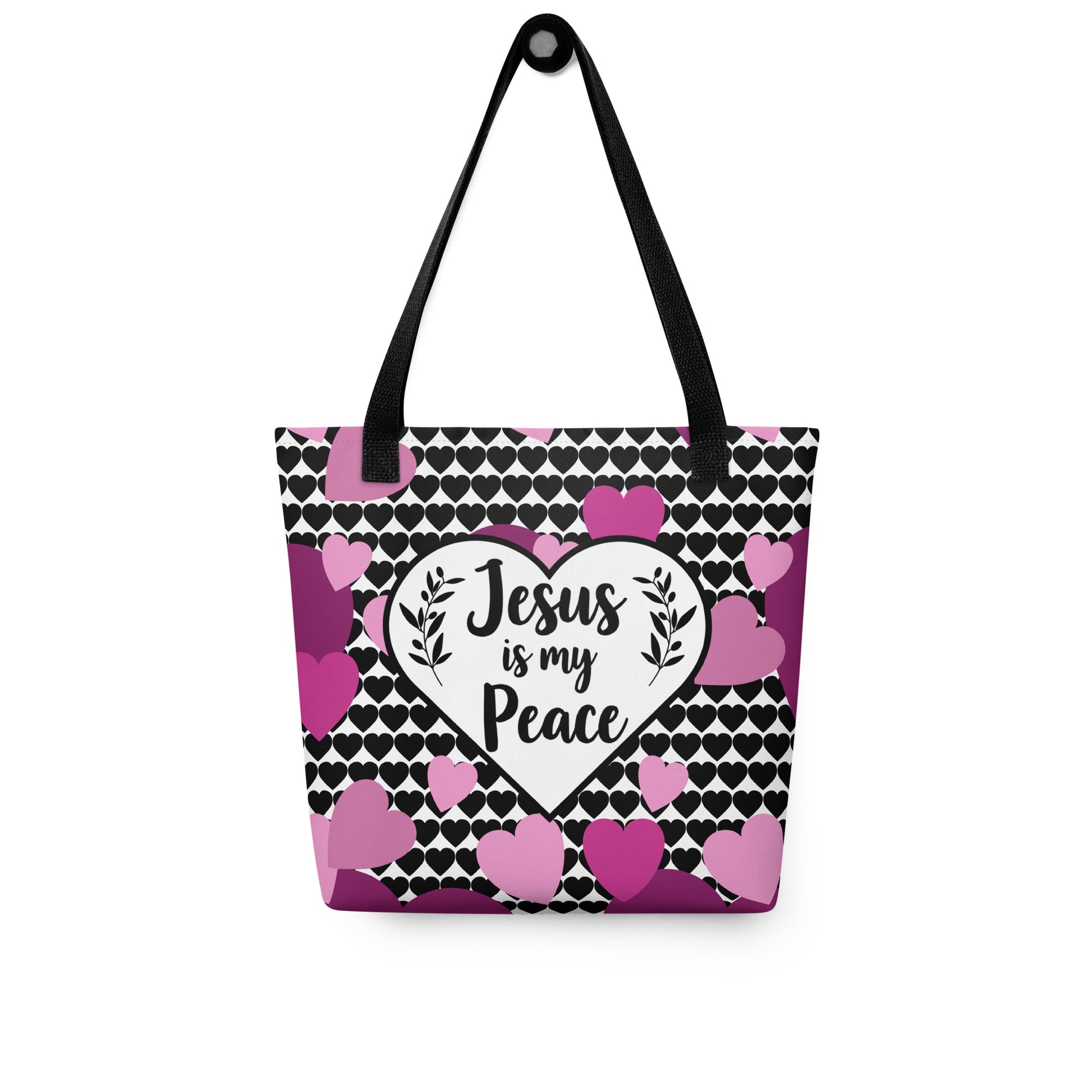 Heart-pattern tote bag with black straps hanging on a hook, featuring a white heart with “Jesus is my Peace” and pink/purple hearts around it.