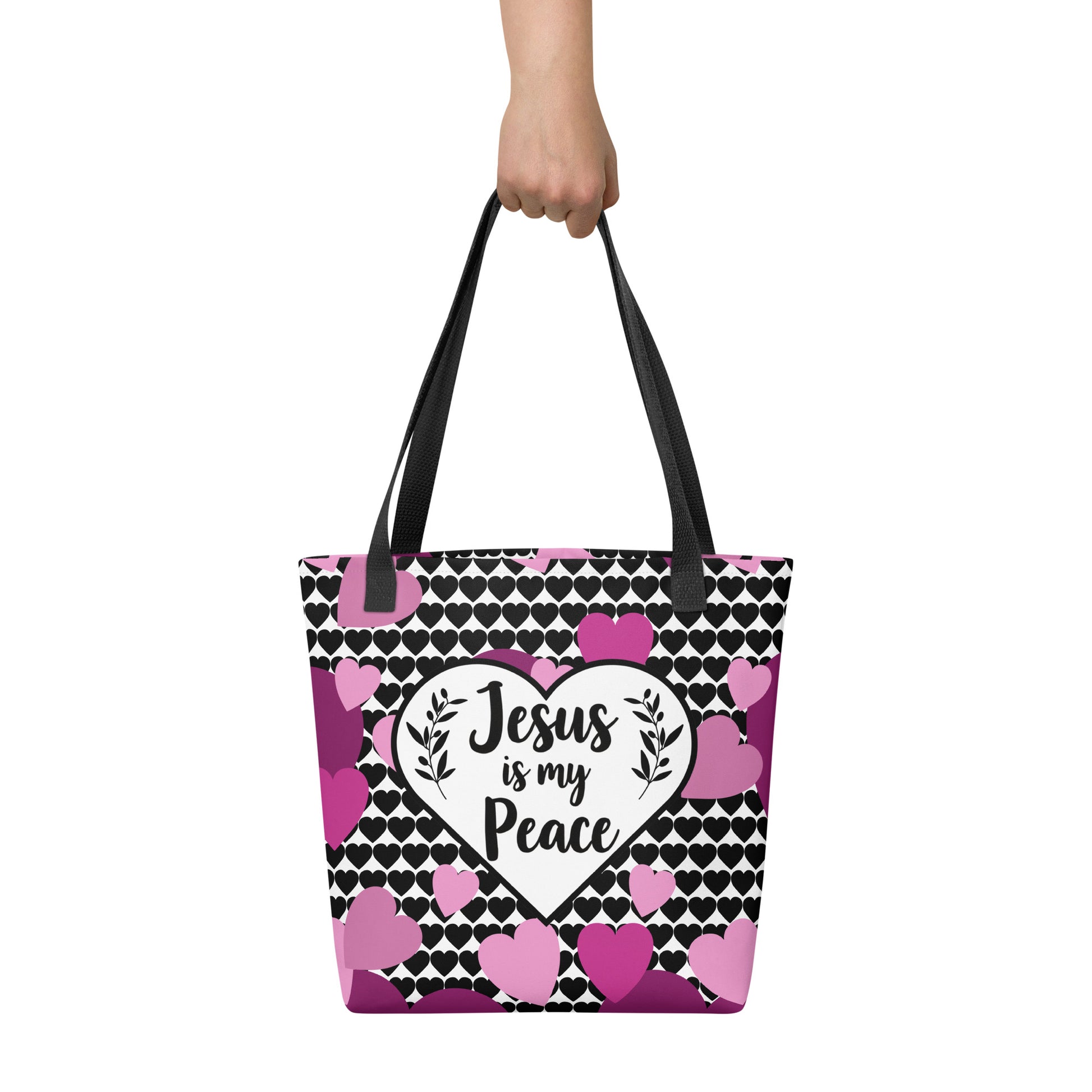 Tote bag held by hand with black straps, displaying a black-and-white heart background and a central “Jesus is my Peace” heart graphic with pink/purple hearts.