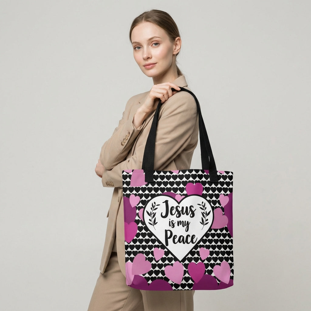 Model carrying a heart-print tote with black straps, featuring the “Jesus is my Peace” design in a white heart with pink and purple hearts.