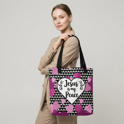 Model carrying a heart-print tote with black straps, featuring the “Jesus is my Peace” design in a white heart with pink and purple hearts.