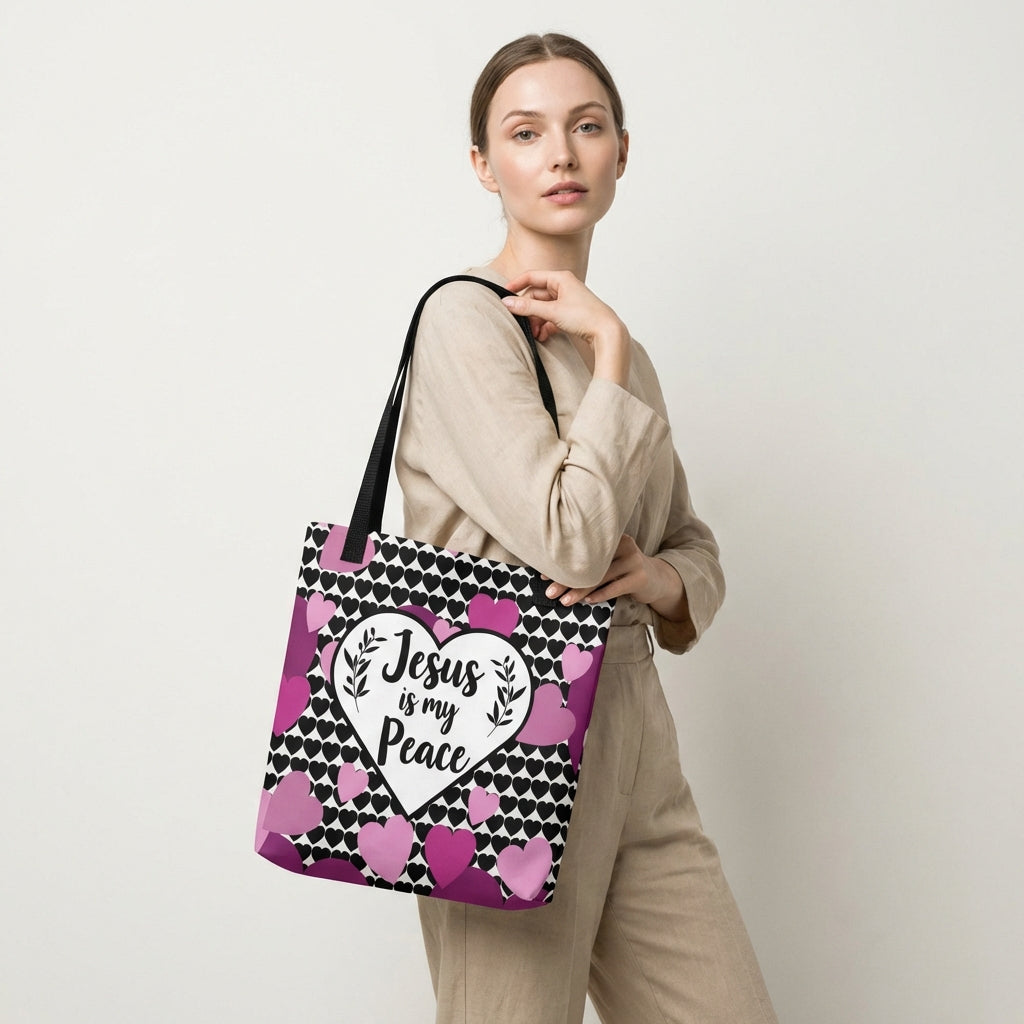 Model carrying a heart-print tote with black straps, featuring the “Jesus is my Peace” design in a white heart with pink and purple hearts.