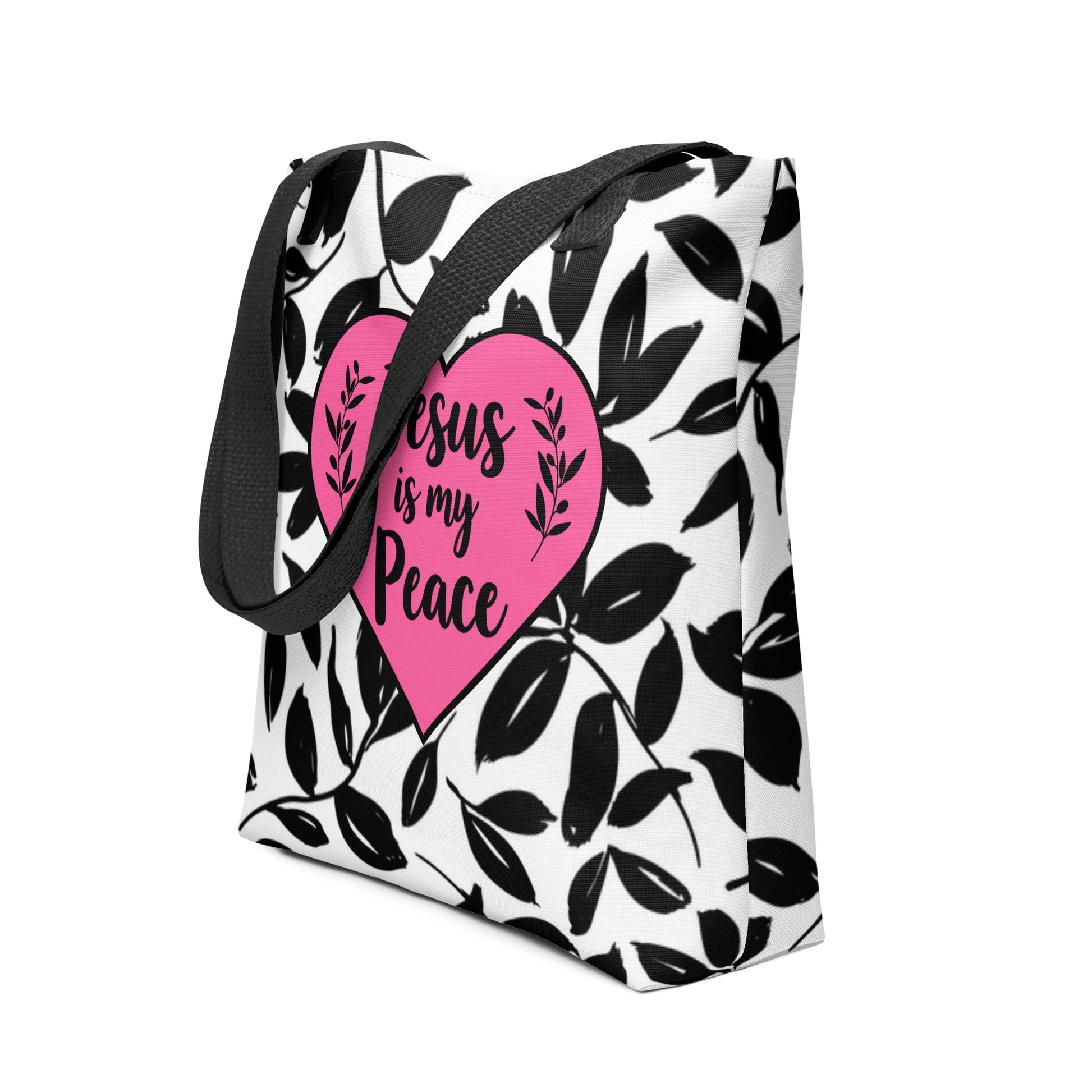 Angled view of patterned tote bag featuring a pink heart design with the phrase “Jesus is my Peace” and black shoulder straps.