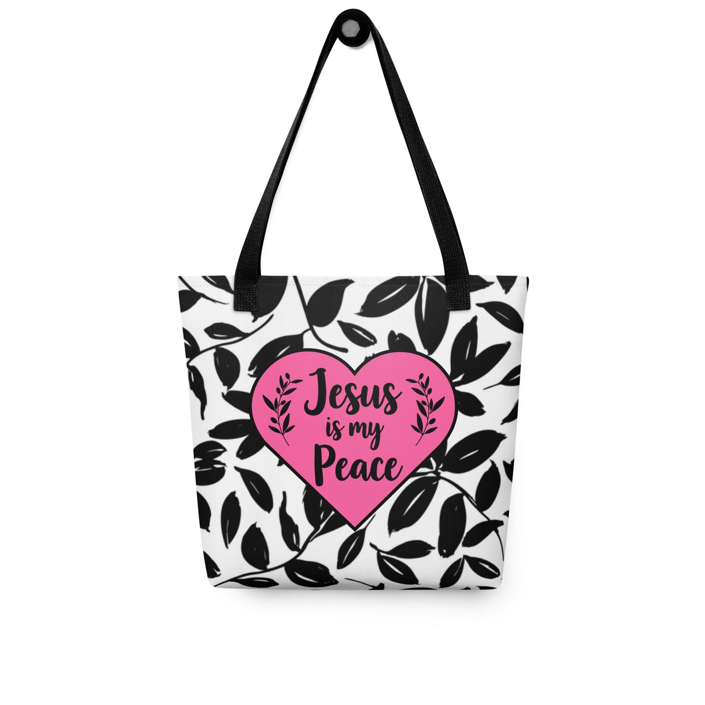 Tote bag hanging by black straps, showing black leaf print and pink heart with “Jesus is my Peace” text.