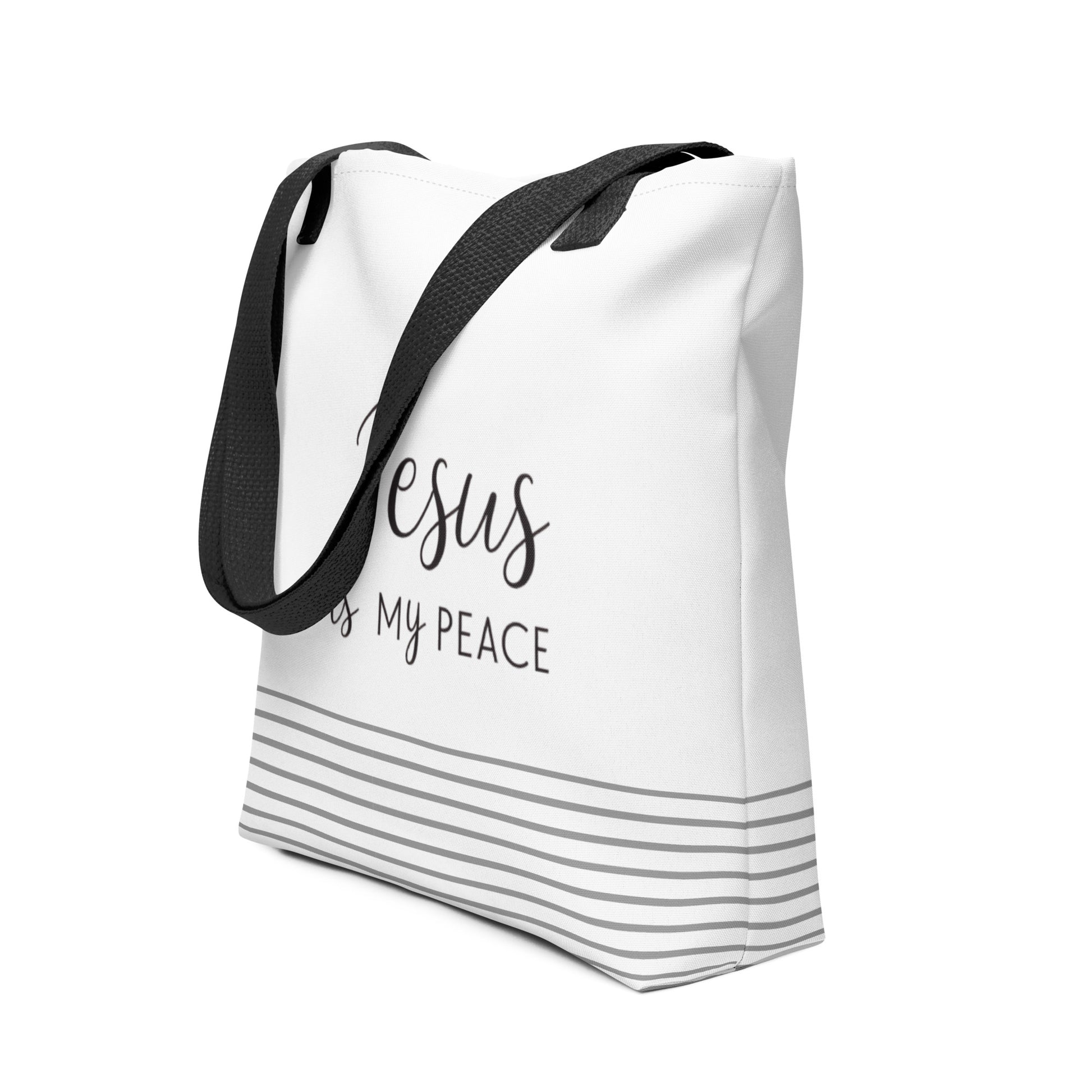 Angled view of a white tote bag with dark gray “Jesus is my peace” lettering and a gray striped base detail.