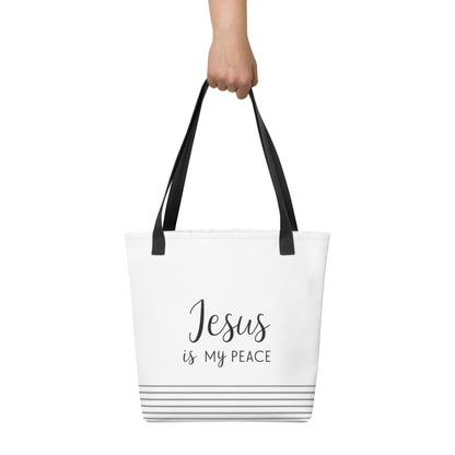 White tote bag held in hand featuring dark gray “Jesus is my peace” text with gray stripe accents near the base.