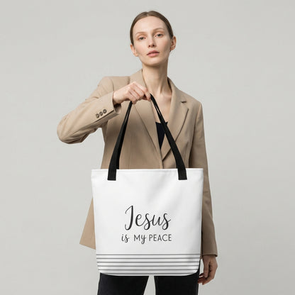 Model holding a white tote bag with black handles that reads “Jesus is my peace” in dark gray with a striped bottom design.