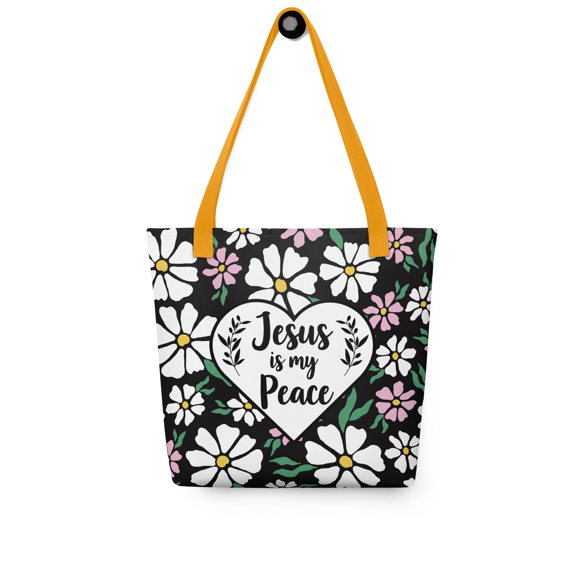 Black floral tote bag with mustard yellow straps hanging on a hook, displaying the white heart with “Jesus is my Peace” on the front.