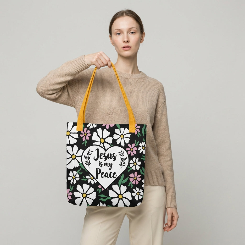 Model carrying a black floral tote with mustard yellow straps and a white heart design that says “Jesus is my Peace.”