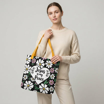 Model carrying a black floral tote with mustard yellow straps and a white heart design that says “Jesus is my Peace.”
