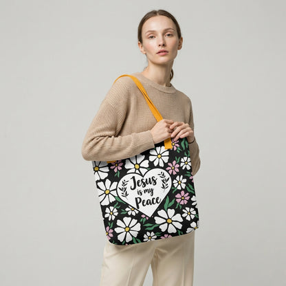 Model carrying a black floral tote with mustard yellow straps and a white heart design that says “Jesus is my Peace.”