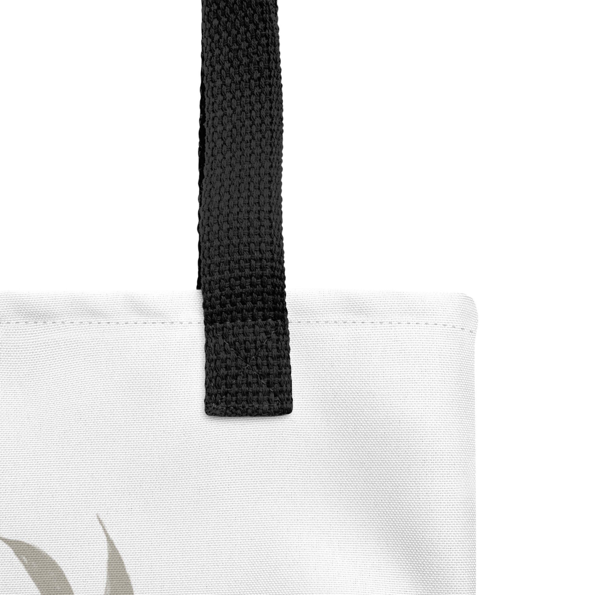 Close-up of the white tote fabric and black strap, highlighting the stitching, textured canvas, and strap weave detail.