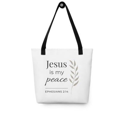 White tote bag hanging on a hook with black handles featuring “Jesus is my peace,” “Ephesians 2:14,” and a leaf design in dark gray.