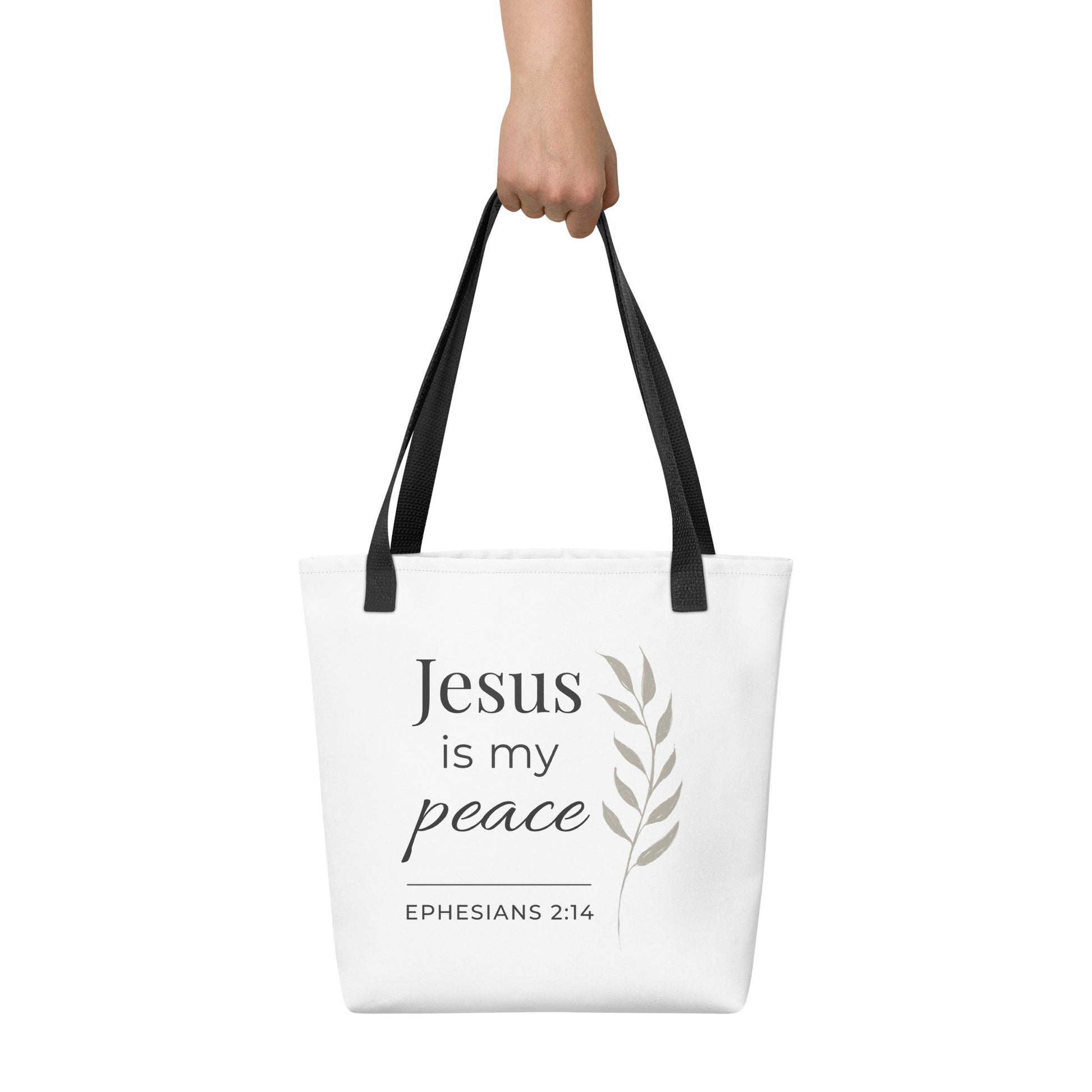 White tote bag held in hand with black handles featuring “Jesus is my peace,” “Ephesians 2:14,” and a leaf design in dark gray.