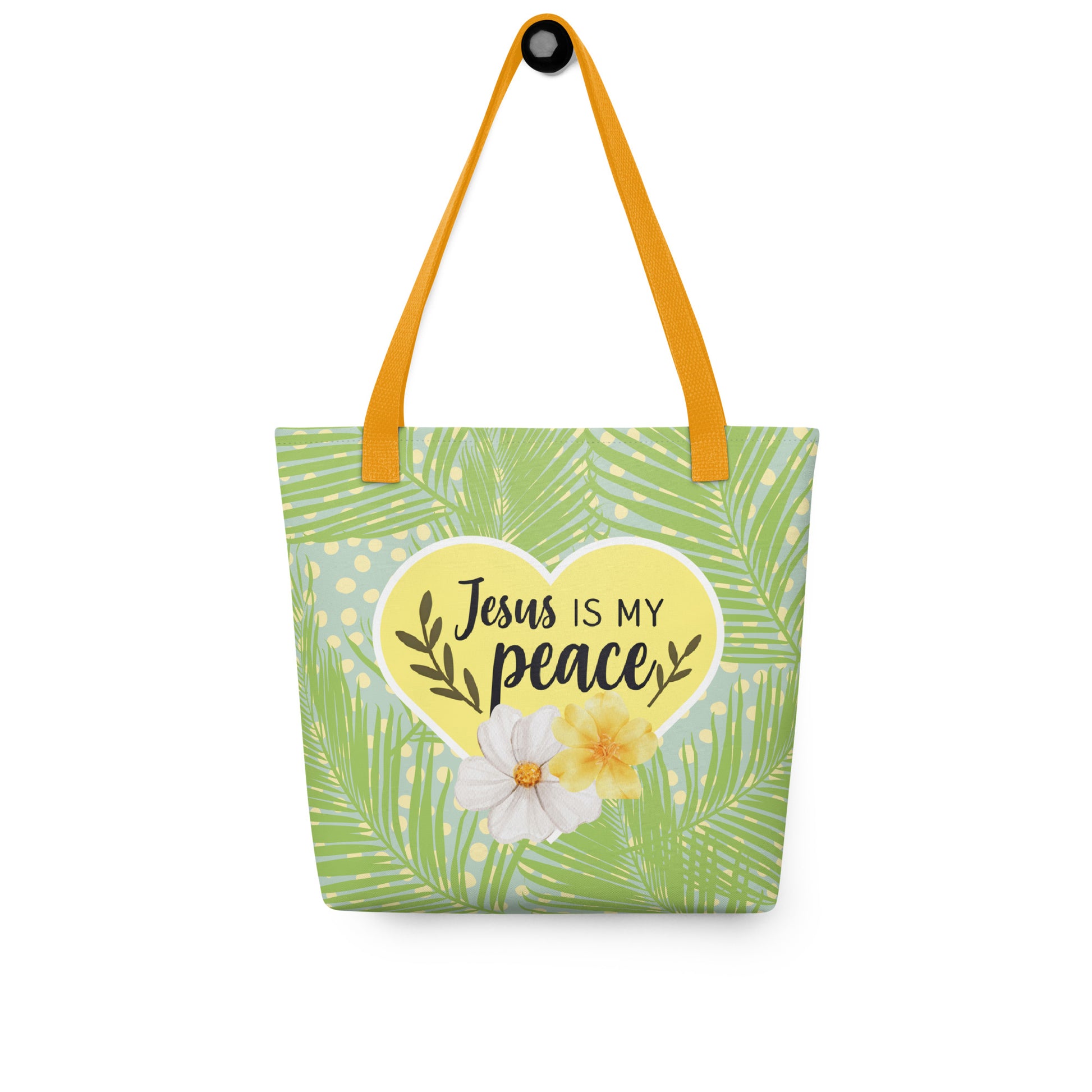 Tote bag hanging on a hook with mustard-yellow straps, green palm fronds and dots, and a yellow heart that says “Jesus is my peace.”