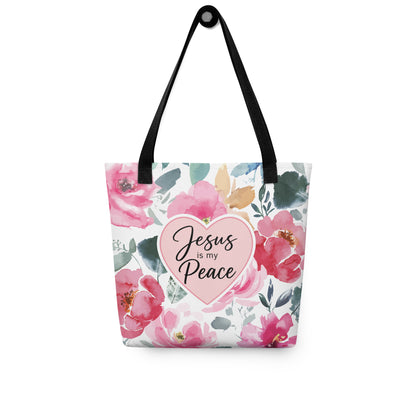 Christian floral tote bag hanging on a hook, featuring black straps, watercolor flowers, green leaves, and “Jesus is my Peace” text.