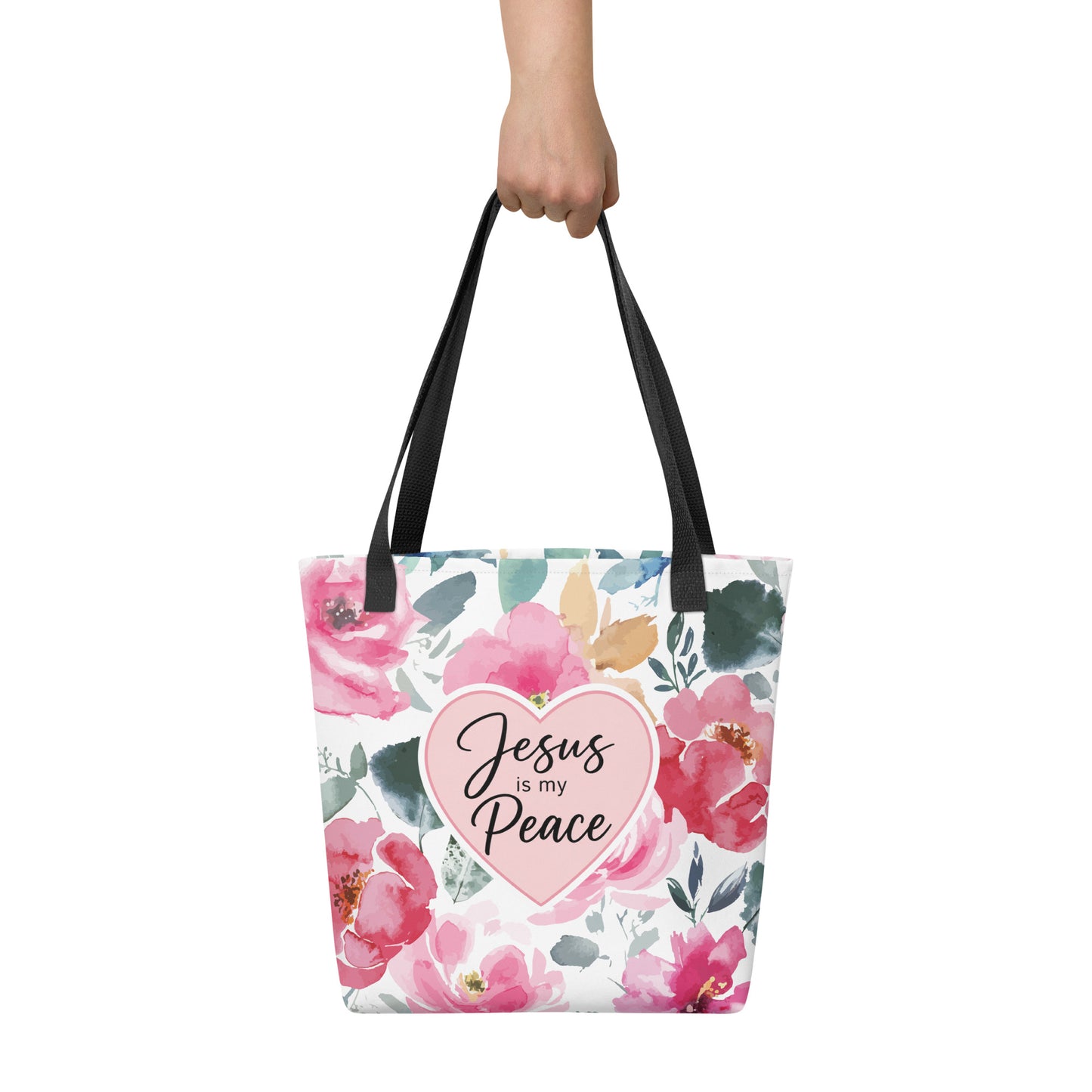 Person holding a floral Christian tote bag with black handles, pink watercolor flowers, and a heart-shaped “Jesus is my Peace” design.