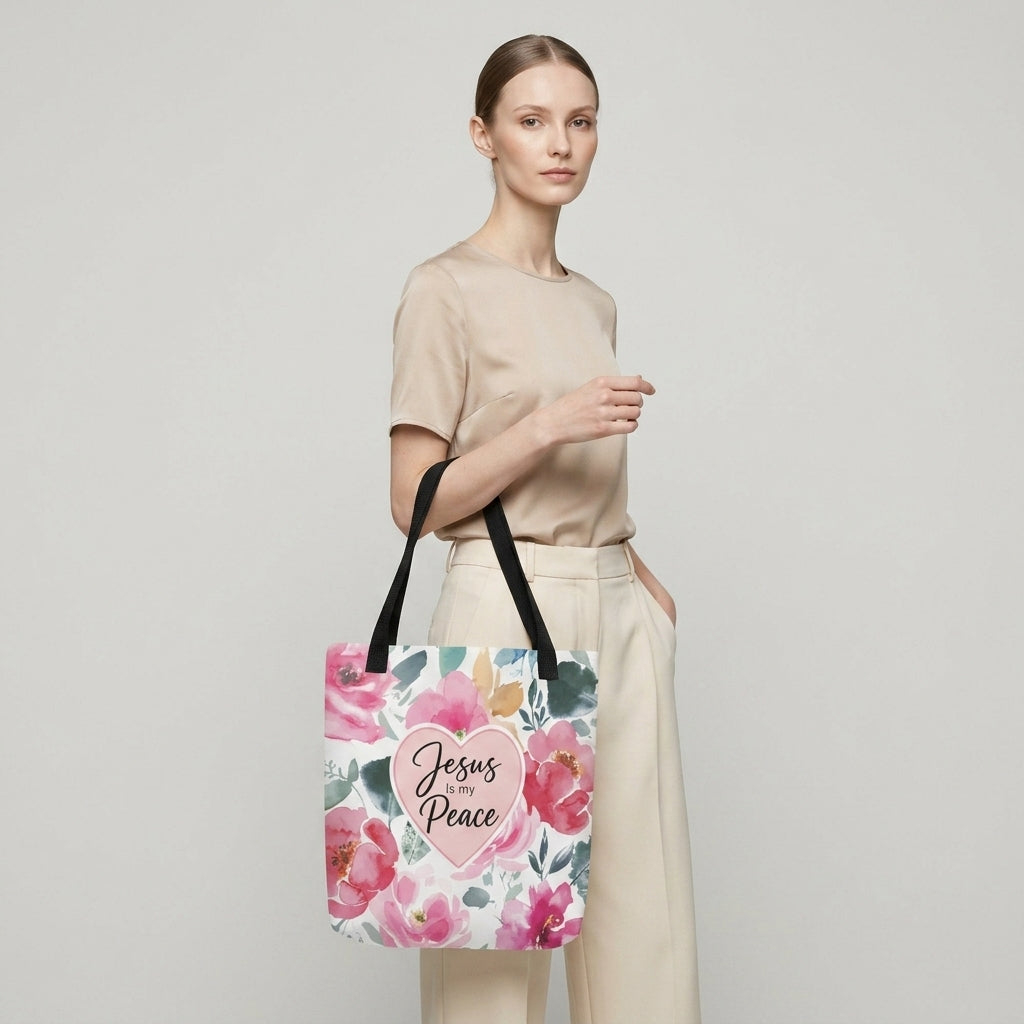 Model carrying a floral Christian tote bag with black handles, pink flower artwork, and a “Jesus is my Peace” heart design.
