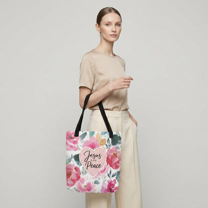Model carrying a floral Christian tote bag with black handles, pink flower artwork, and a “Jesus is my Peace” heart design.