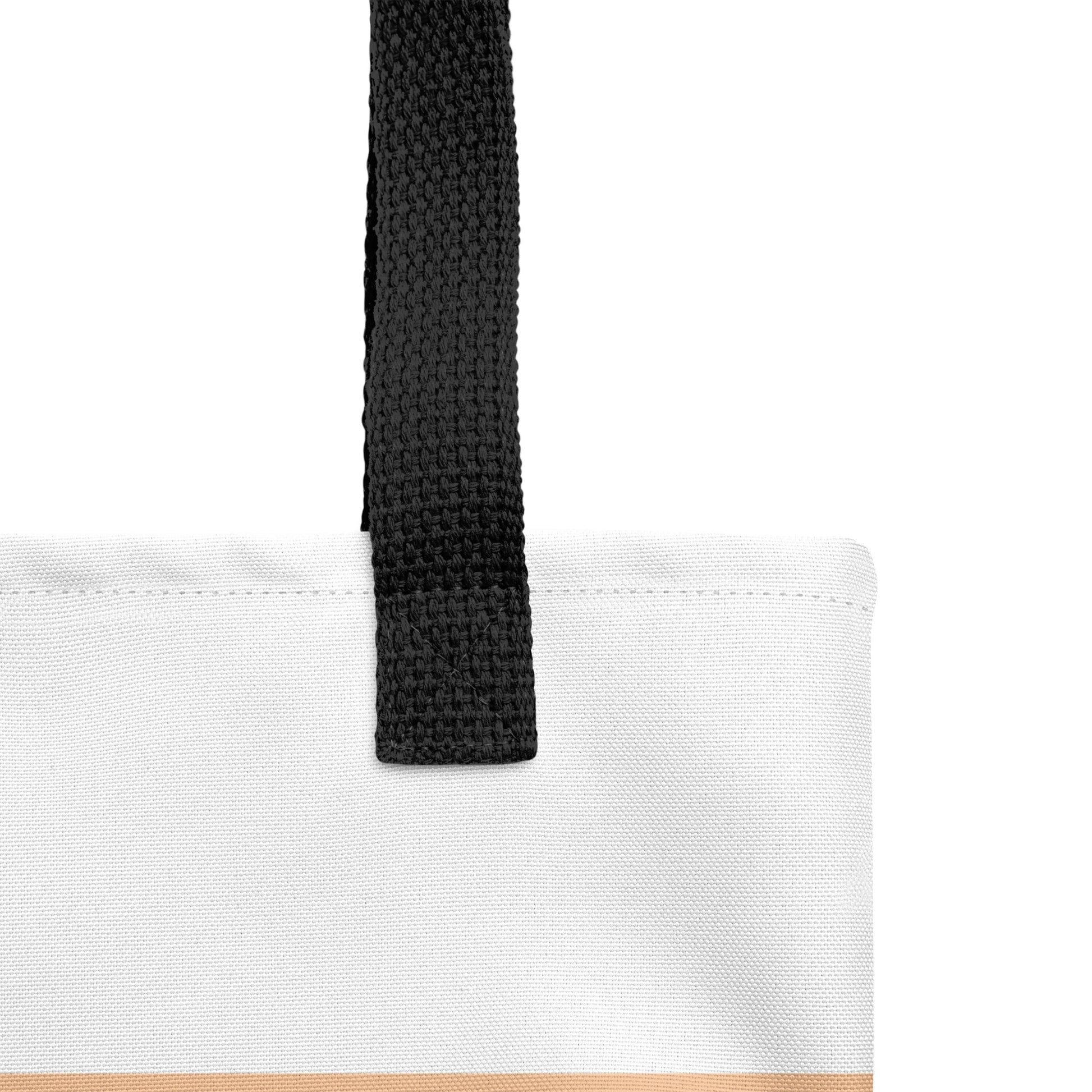Close-up of a geometric Christian tote bag showing the black woven handle, fabric texture, stitching, and white and peach color-block design.