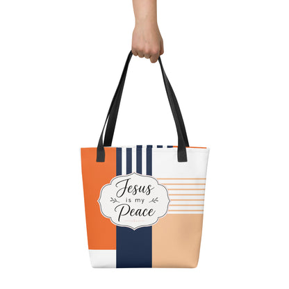 Person holding a geometric Christian tote bag with black handles, warm orange and peach tones, navy accents, and “Jesus is my Peace” text.