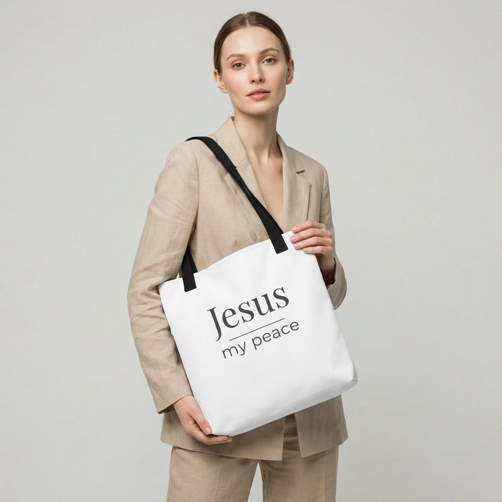 Lifestyle photo of a model holding a white tote bag with black handles featuring the text “Jesus my peace” in dark gray.