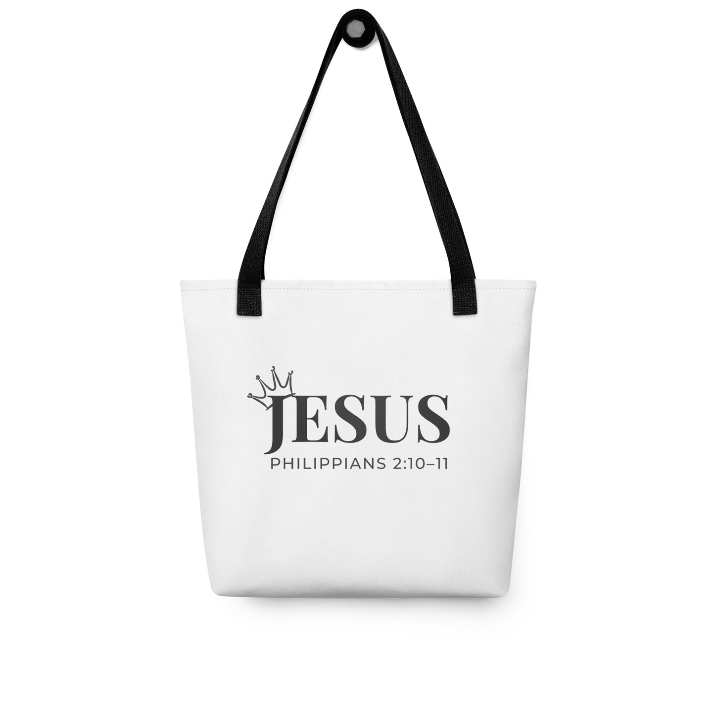 White tote bag hanging on a hook printed with “JESUS” and “Philippians 2:10–11,” with a small crown design.