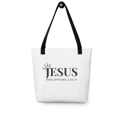 White tote bag hanging on a hook printed with “JESUS” and “Philippians 2:10–11,” with a small crown design.