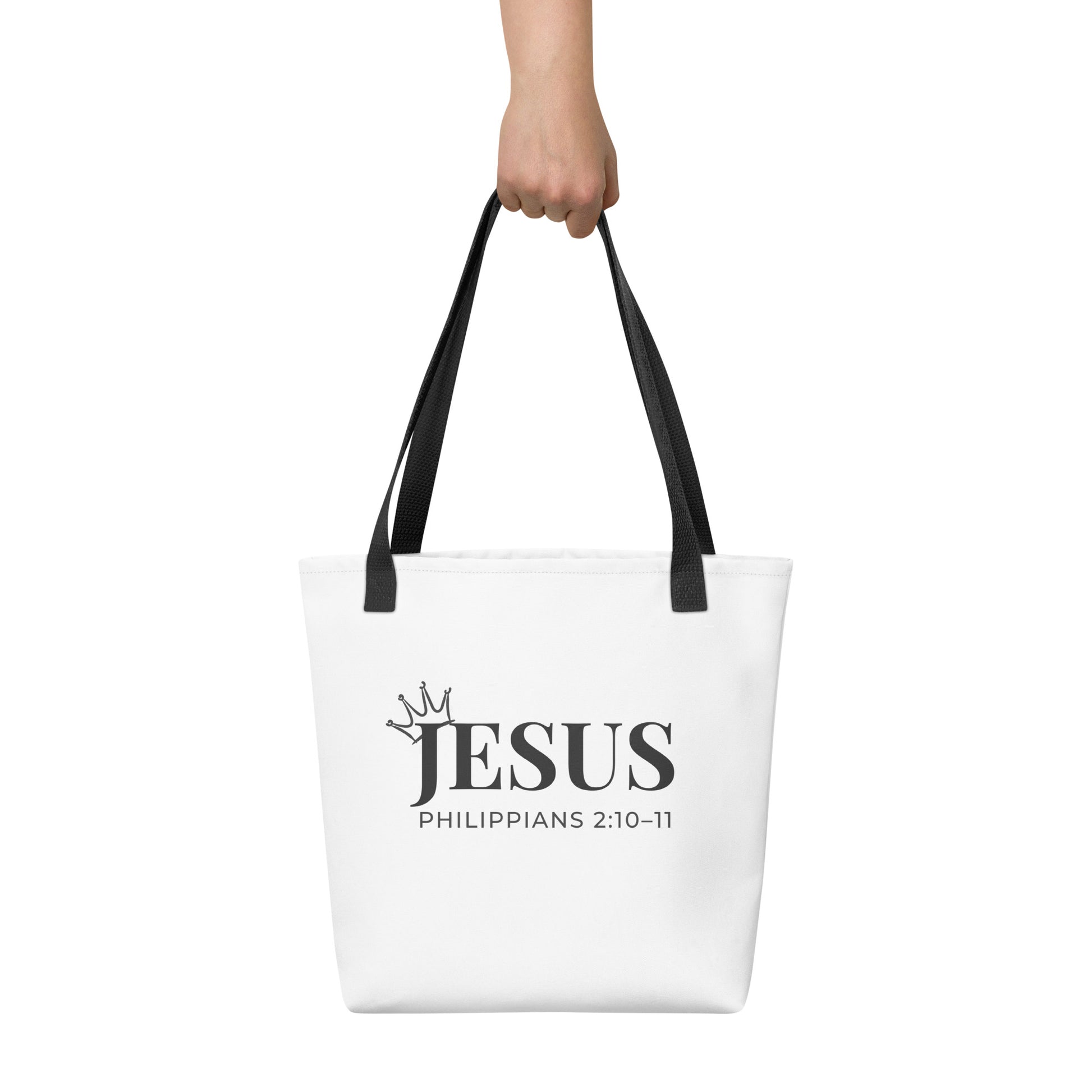 White tote bag held in hand featuring “JESUS” in large black letters with a crown graphic and Philippians 2:10–11.