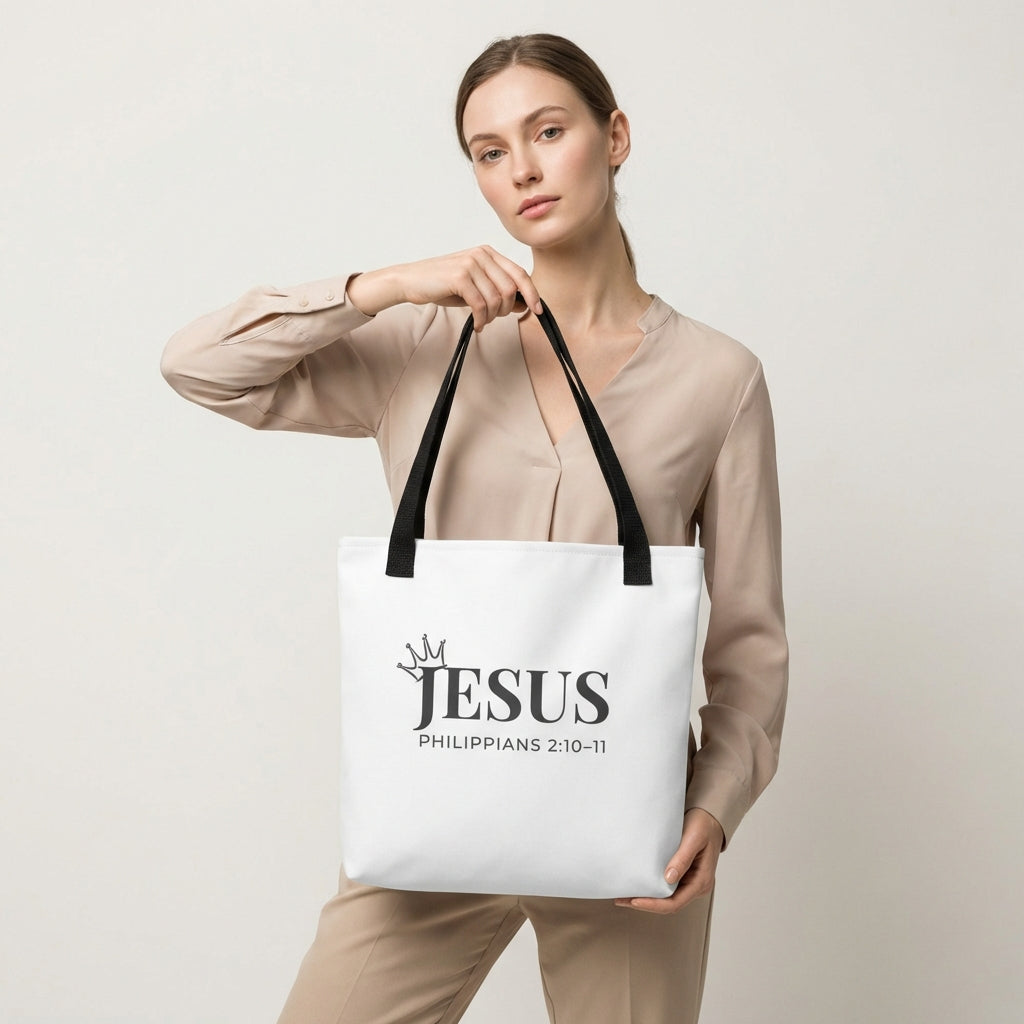 Model holding a white tote bag featuring “JESUS,” crown icon, and “Philippians 2:10–11.”