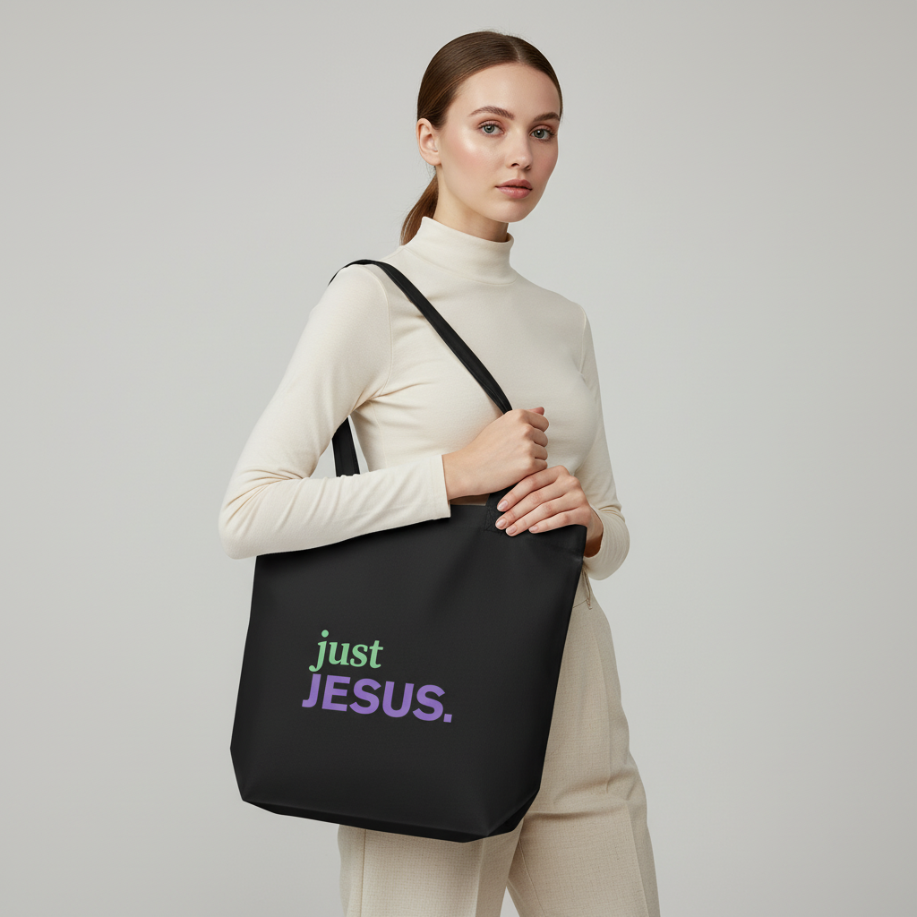 Model holding a black cotton tote bag with the “just JESUS.” design in green and purple text.