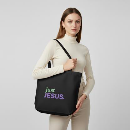 Model holding a black cotton tote bag with the “just JESUS.” design in green and purple text.