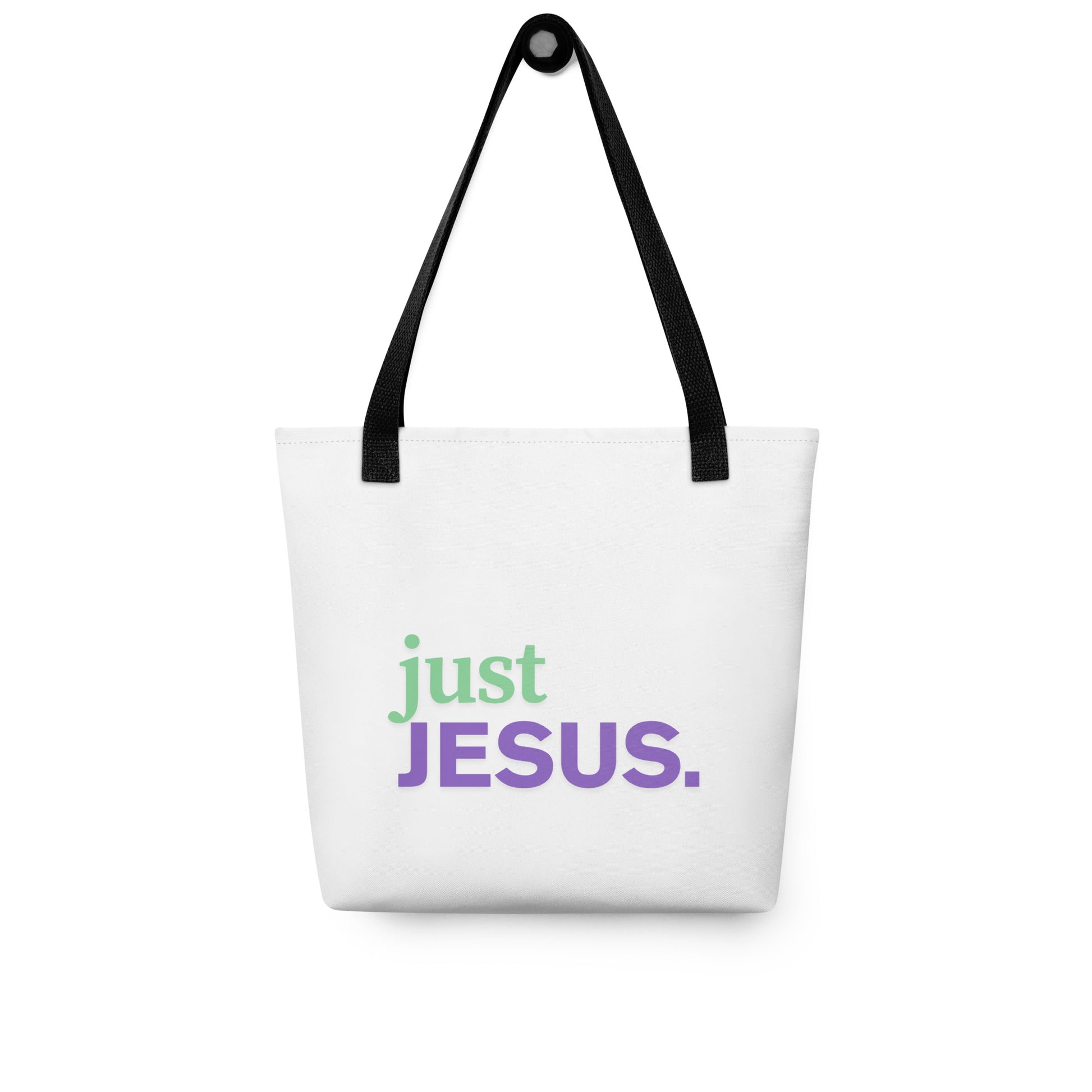 White tote bag hanging on a hook with black handles and “just JESUS.” printed in green and purple.
