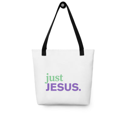White tote bag hanging on a hook with black handles and “just JESUS.” printed in green and purple.