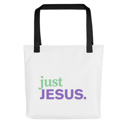 Front view of a white tote bag with black handles featuring “just JESUS.” in green and purple lettering.
