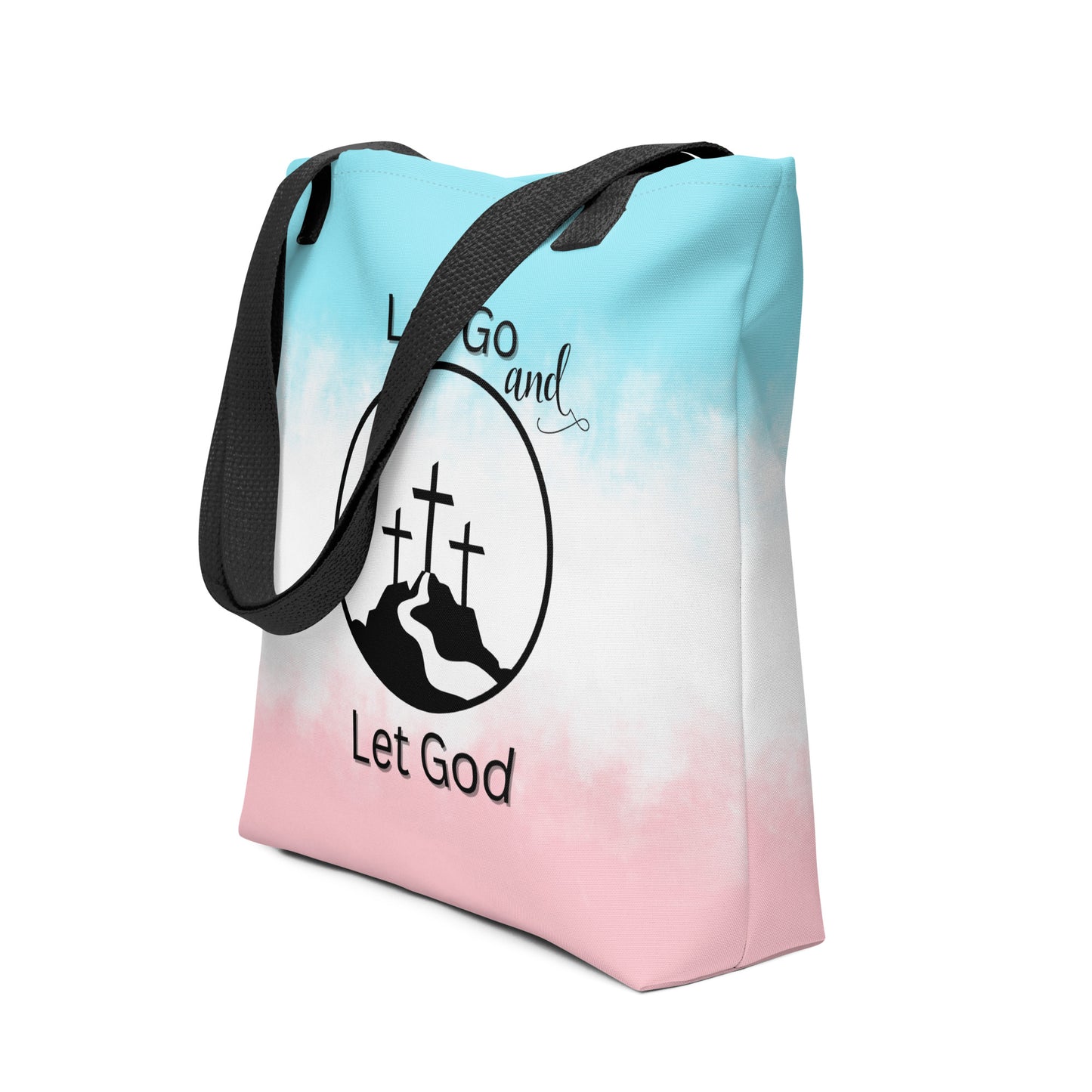 Angled view of a tote bag with black handles featuring a blue-to-pink gradient and “Let Go and Let God” design with crosses on a mountain.