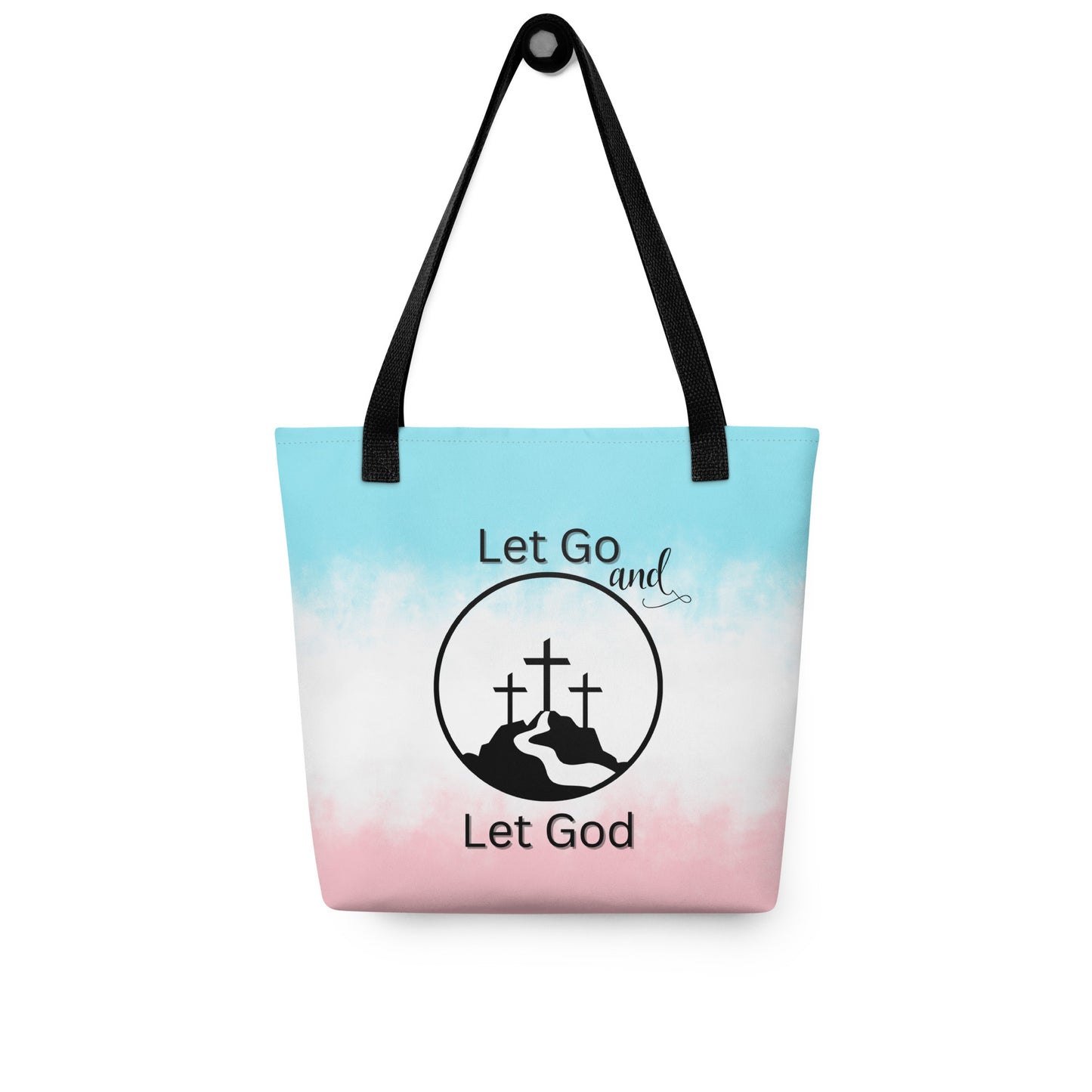 Tote bag hanging on a hook with black handles, a soft blue-to-pink gradient, and “Let Go and Let God” cross-and-mountain artwork.
