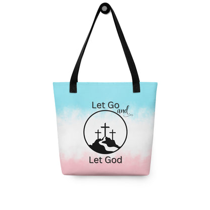 Tote bag hanging on a hook with black handles, a soft blue-to-pink gradient, and “Let Go and Let God” cross-and-mountain artwork.