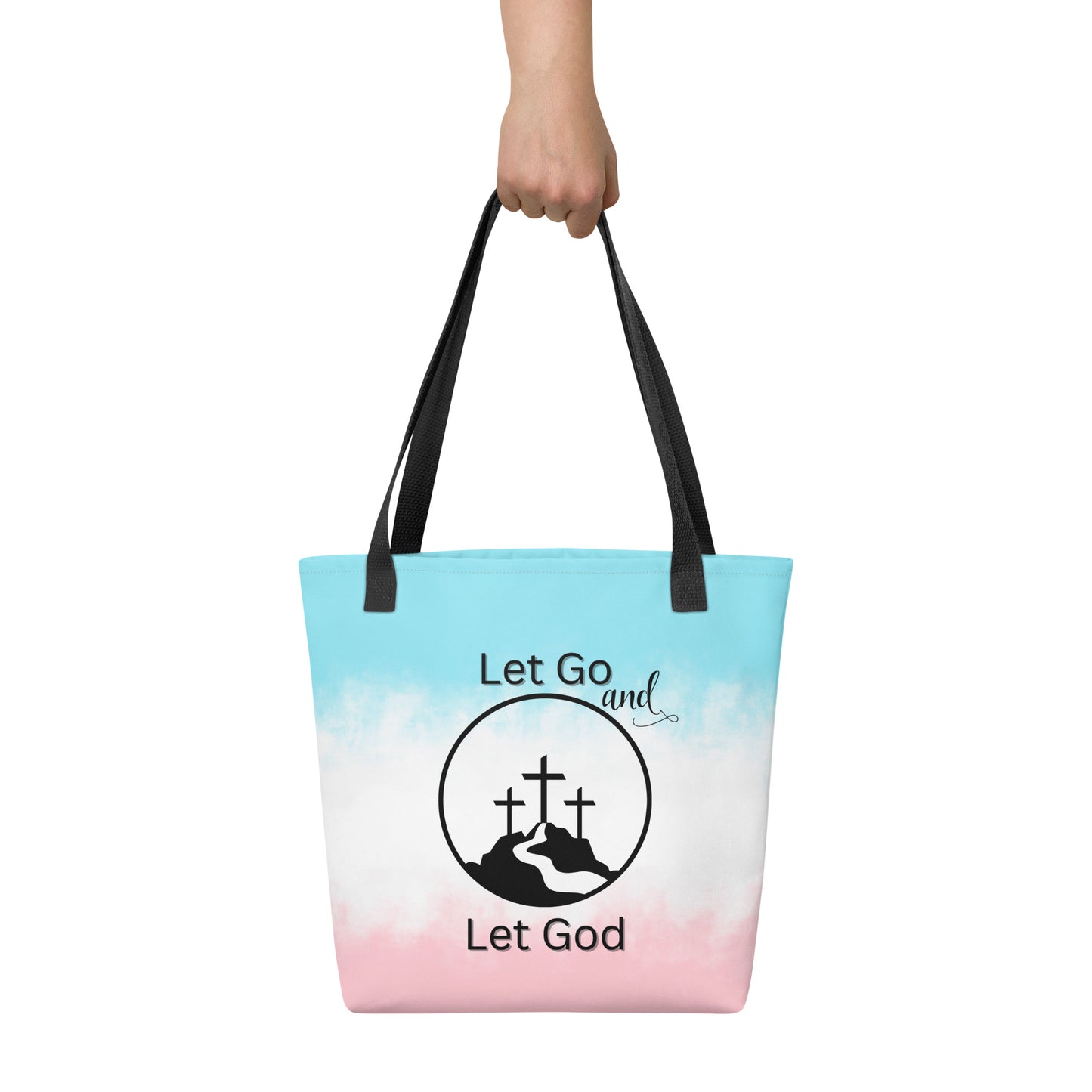 Tote bag held in hand with black handles, a pastel blue-to-pink gradient, and “Let Go and Let God” with a mountain and cross graphic.