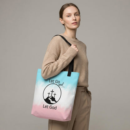 Model holding a tote bag with black handles featuring a blue-to-pink gradient and “Let Go and Let God” cross-and-mountain design.