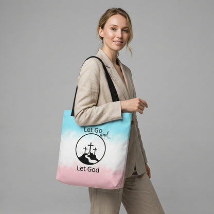 Model holding a tote bag with black handles featuring a blue-to-pink gradient and “Let Go and Let God” cross-and-mountain design.