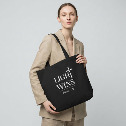 Lifestyle photo of a model holding a black tote bag featuring “Light Wins,” a cross graphic, and “John 1:5.”