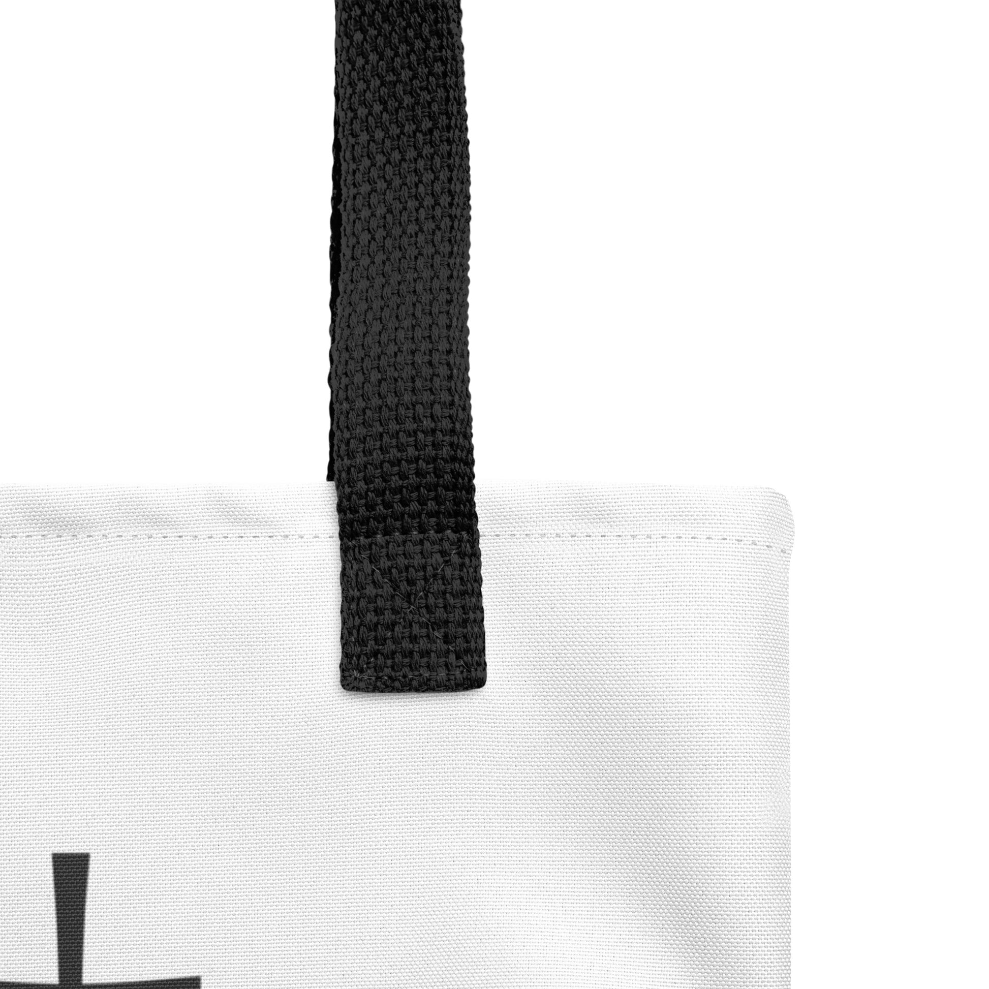 Close-up of the white tote fabric and black strap, highlighting the stitching, textured canvas, and strap weave detail.