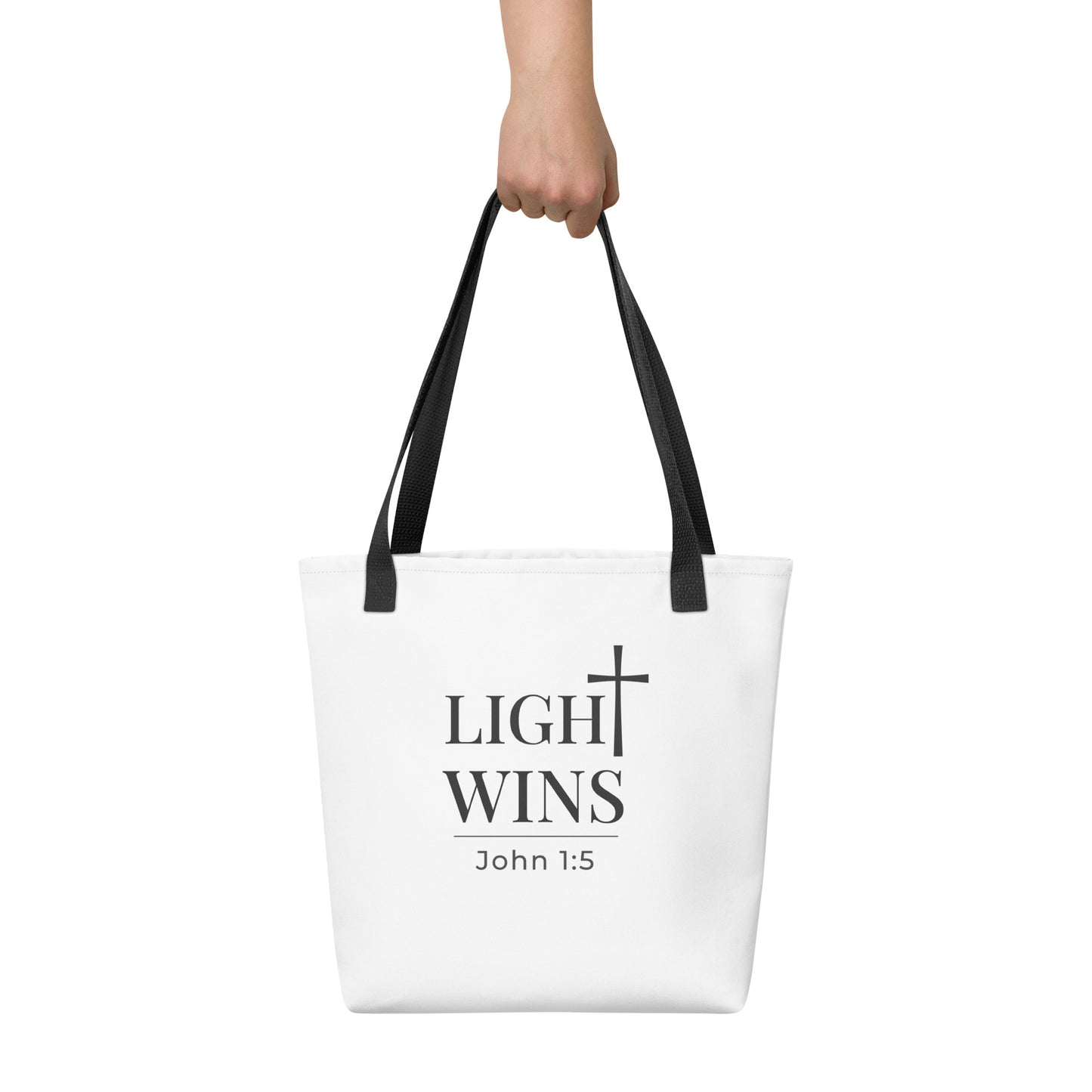White tote bag held in hand featuring dark gray “Light Wins” text, cross symbol, and “John 1:5” underneath.
