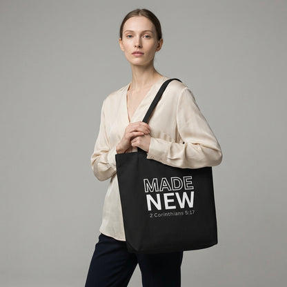 Model holding a black cotton tote bag printed with “MADE NEW” and “2 Corinthians 5:17” in white text.