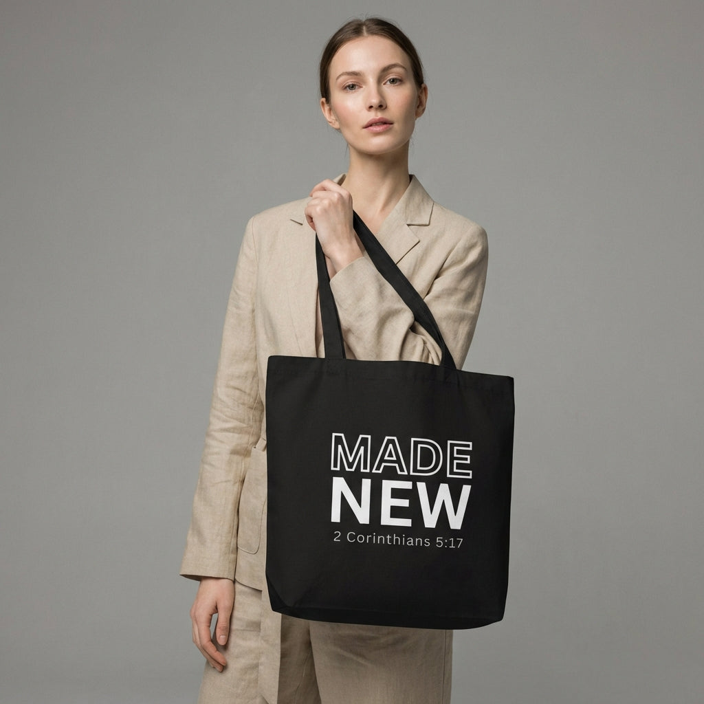 Model holding a black cotton tote bag printed with “MADE NEW” and “2 Corinthians 5:17” in white text.