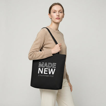 Model holding a black cotton tote bag printed with “MADE NEW” and “2 Corinthians 5:17” in white text.